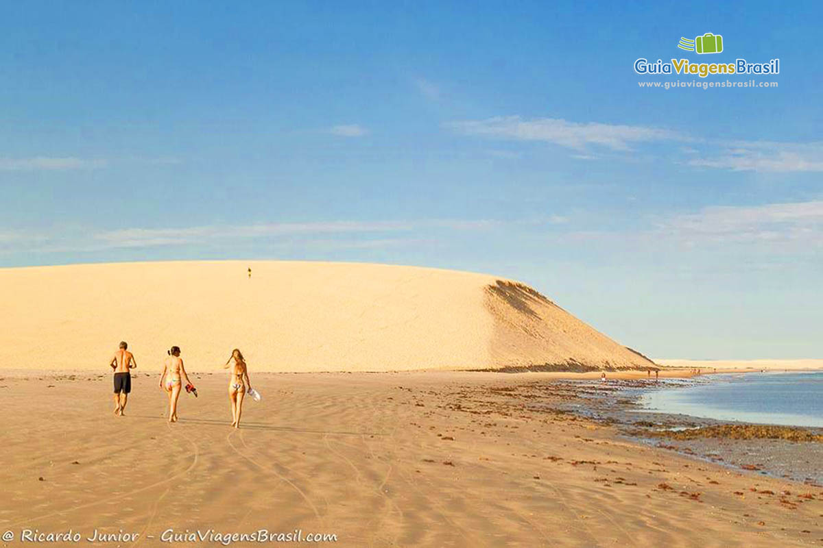 Imagem de pessoas caminhando na praia em direção as dunas.